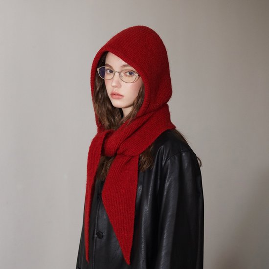 Model met bril en bruin haar draagt een rode, geribbelde gebreide sjaal met capuchon en een zwarte leren jas.