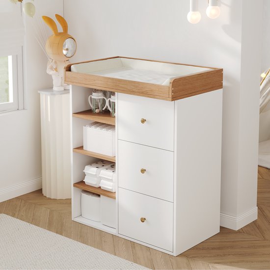 Babycommode met wit frame, houten blad en aankleedkussen, voorzien van drie lades en open planken aan de zijkant.