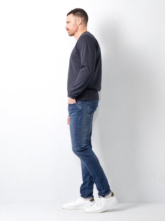 Man in donkerblauwe slim fit jeans, gezien vanaf de zijkant.