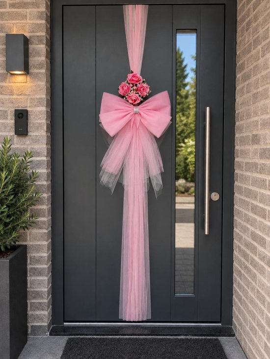 Roze tule strik met roze kunstrozen en strass accent, gedrapeerd aan een donkergrijze voordeur.
