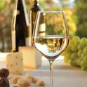 Verre de vin blanc avec en arrière-plan deux bouteilles, du fromage et des raisins.