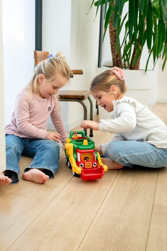 Twee meisjes spelen met een rode, groene en gele vuilniswagen op de vloer.