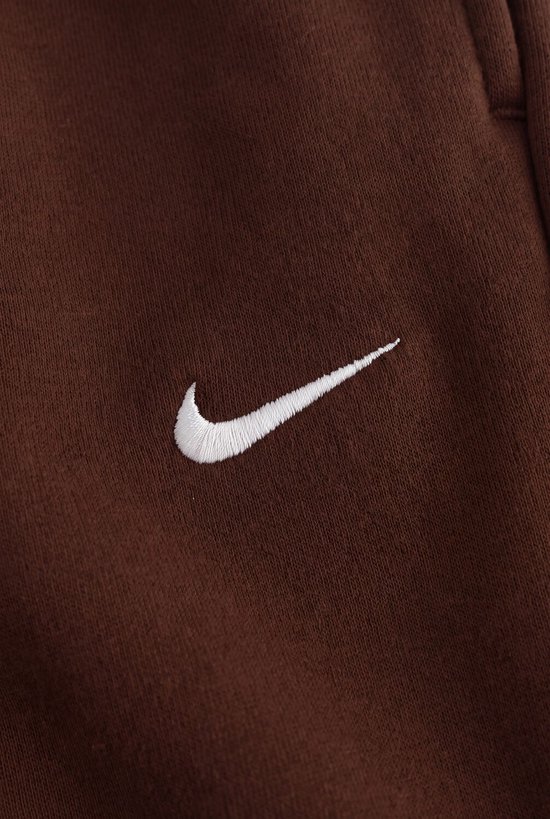 Detail van het witte Nike logo op een bruine Nike broek.