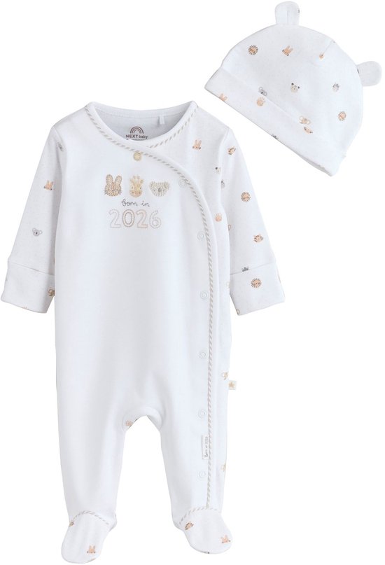 Witte babypyjama met lange mouwen en bijpassende muts, beide met een stipjespatroon en dierenprints. De pyjama heeft 'Born in 2026' geborduurd.