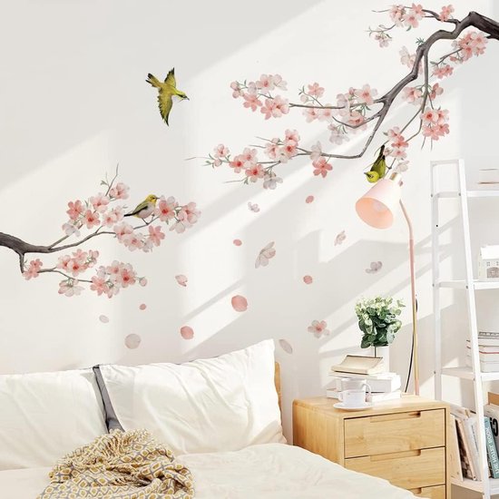 Décoration de chambre avec branches de fleurs roses et oiseaux jaunes, au-dessus d'un lit et d'une table de chevet.