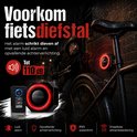 Zwart fietsalarm met rode ring en afstandsbediening naast fiets in steeg, met icoons voor alarm, licht, waterdichtheid.