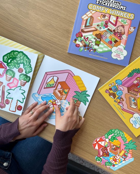 Bovenaanzicht van een tafel met drie 'Cozy & Cute Stickerrooms' boeken, waarvan één geopend met een sticker die in een zwembadscene wordt geplakt.