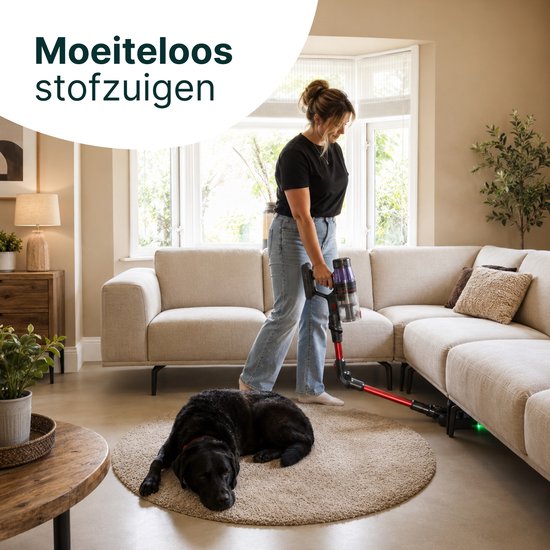 Vrouw stofzuigt woonkamer met rode en zwarte steelstofzuiger, hond ligt op een rond kleed.