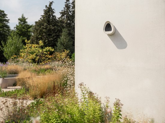 Witte vogelvoerder aan een lichte muur in een tuin.