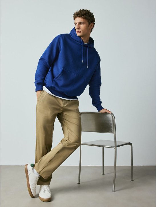 Man met zandkleurige chino en blauwe hoodie, leunend op stoel