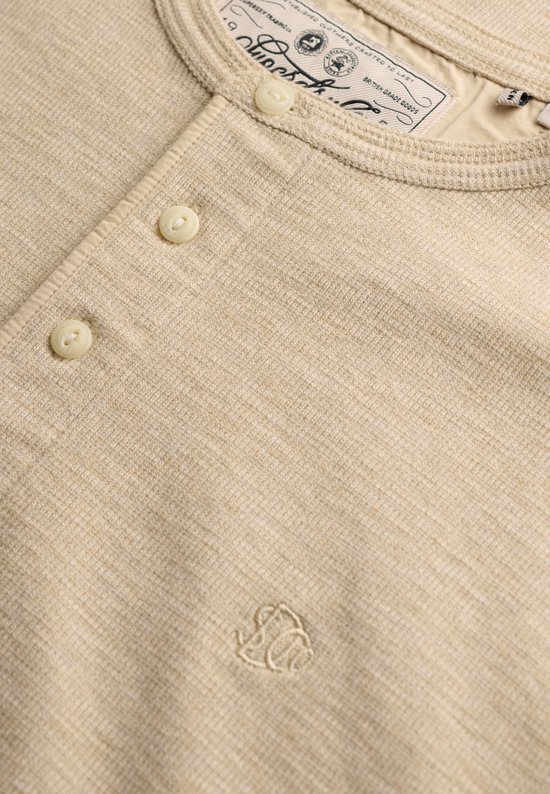 Close-up van een beige waffle-structuur top met knoopsluiting en geborduurd Superdry-logo op de borst.