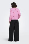 Model draagt achterkant roze trui met rode hartjesprint, lange mouwen en ronde hals, met zwarte broek.