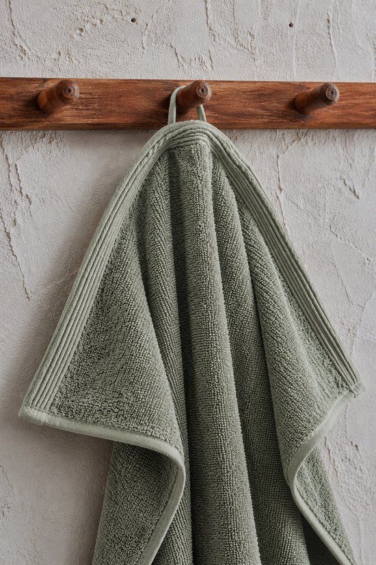 Een sagegroene handdoek hangt aan een houten kapstok met drie haken.