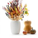Een vaas met een herfstboeket met gele pluimen, rode bloemen en gedroogde zonnebloemen, naast pompoenen.