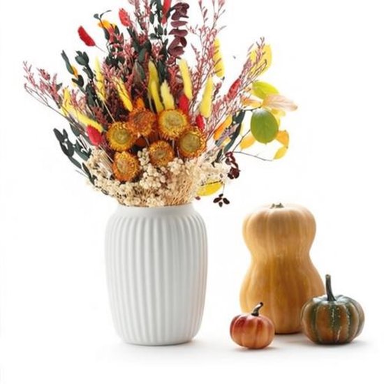 Een vaas met een herfstboeket met gele pluimen, rode bloemen en gedroogde zonnebloemen, naast pompoenen.
