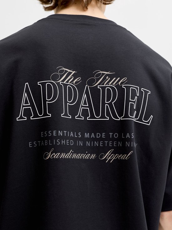 Close-up van rug van zwart t-shirt met opdruk 'The True Apparel Essentials Made to Last Established in Nineteen Ninety Scandinavian Appeal'.