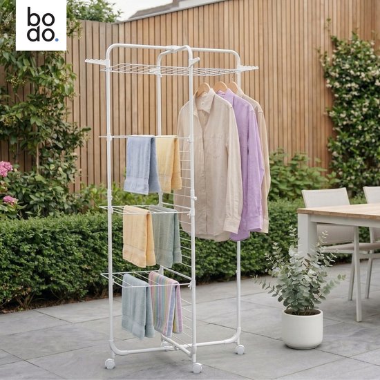 Een vrouw hangt kleding aan een witte droogtoren met vier niveaus op een terras.