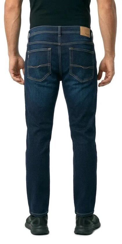 Man met de rug naar de camera, draagt een donkerblauwe slim fit spijkerbroek met gele stiksels en merkembleem op de achterzak.
