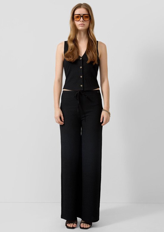 Model in zwarte tweedelige outfit: cropped vest met knopen en wijde broek met trekkoord, zonnebril.