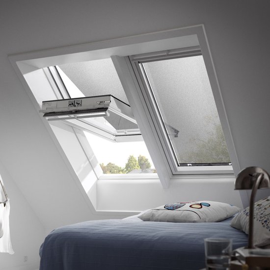 Store pare-soleil noir pour une fenêtre de toit dans une chambre, partiellement déroulé au-dessus d'un lit.