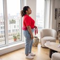 Vrouw met rode top en spijkerbroek draagt een rood warmtekussen om haar onderrug.