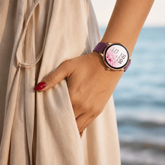 Paarse smartwatch met rosegouden kast, gedragen door een vrouw met een lichte jurk, met bloemen op het scherm.