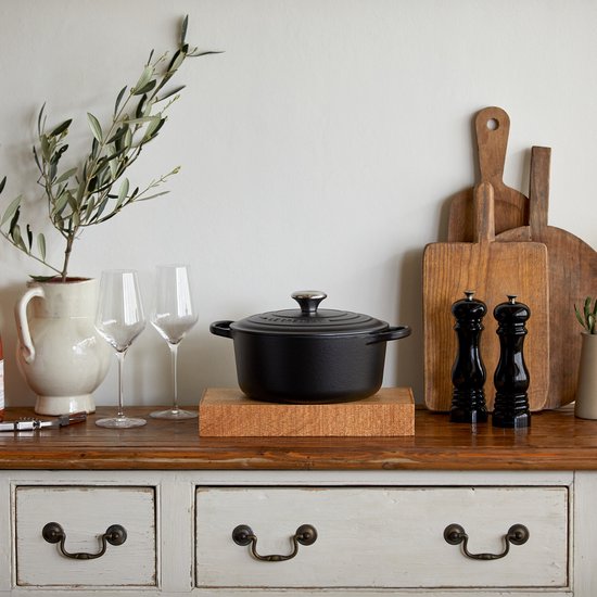 Zwarte Le Creuset braadpan op een houten onderzetter, in een keukenhoek.