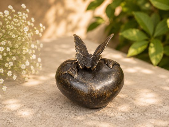 Bronzen hartvormige urn met vlinder, naast witte bloesems en groen blad.