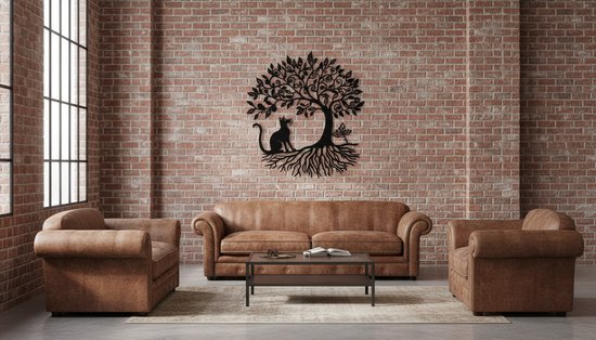 Zwarte metalen wanddecoratie van een levensboom met een kat en vlinder, hangend aan een bakstenen muur boven een bruine lederen bank.