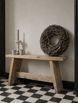 Een houten bankje met een kandelaar, twee potjes en een krans ernaast, op een zwart-wit geblokte vloer.