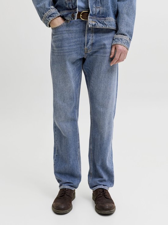Een man draagt een spijkerbroek in een medium wassing met een bruine leren riem en donkere schoenen.