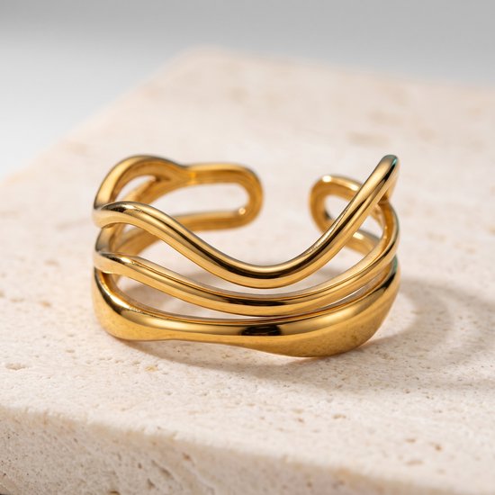 Bague dorée aux fils ondulés superposés et extrémités ouvertes, sur un support en pierre.