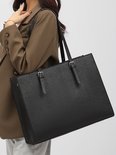 Een vrouw draagt een zwarte, getextureerde laptoptas met een bruine blazer.