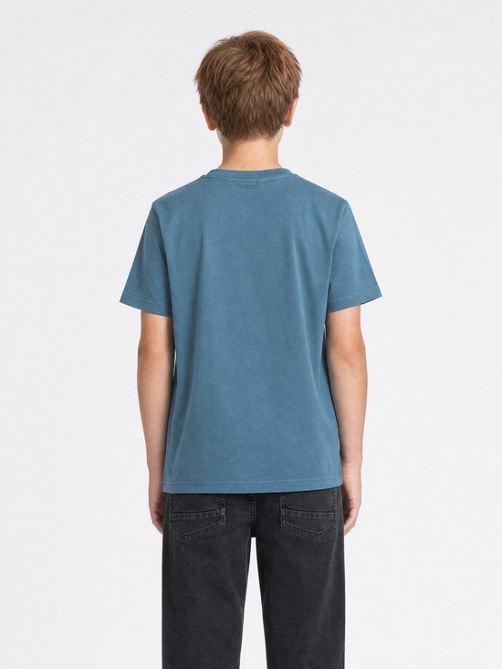 Achterkant van een jongen die een effen blauw katoenen T-shirt met korte mouwen en zwarte jeans draagt.