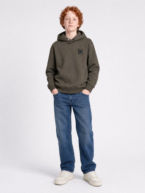 Jongen met krullend rood haar in een donkergroene hoodie met een zwart logo op de linkerborst, en een blauwe jeans.