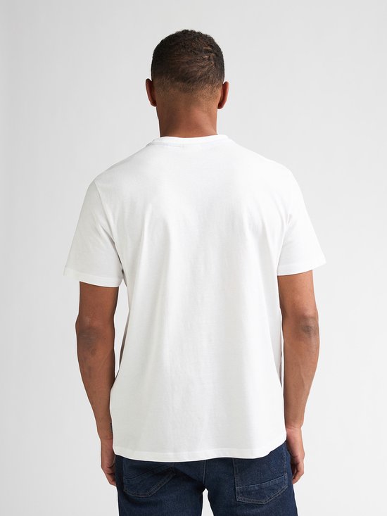 Man met donker haar, draagt een wit T-shirt en spijkerbroek, achterkant.