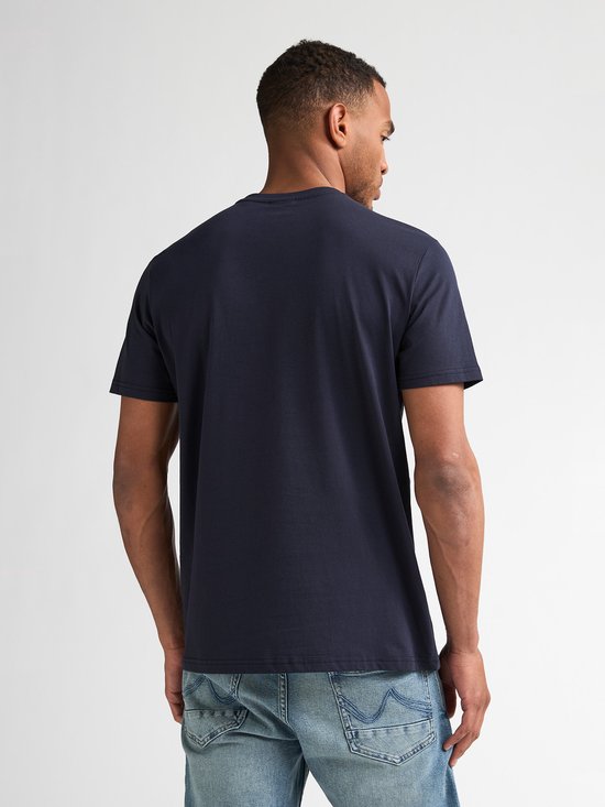 Model van achteren gezien, draagt een marineblauw T-shirt en een spijkerbroek.