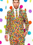 Man in een kleurrijk confettipak, met een witte shirt en stropdas, tegen een witte achtergrond met confetticirkels.