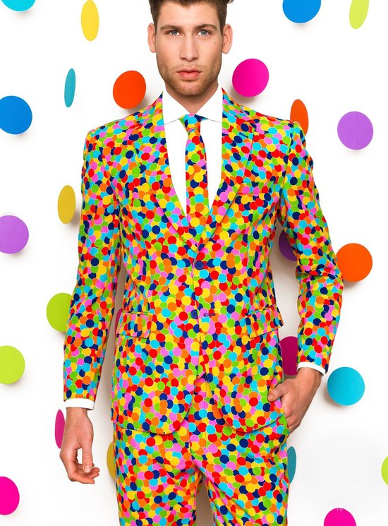 Man in een kleurrijk confettipak, met een witte shirt en stropdas, tegen een witte achtergrond met confetticirkels.