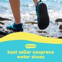 Voeten in blauwe Waimea waterschoenen lopen op een kiezelstrand bij het water.