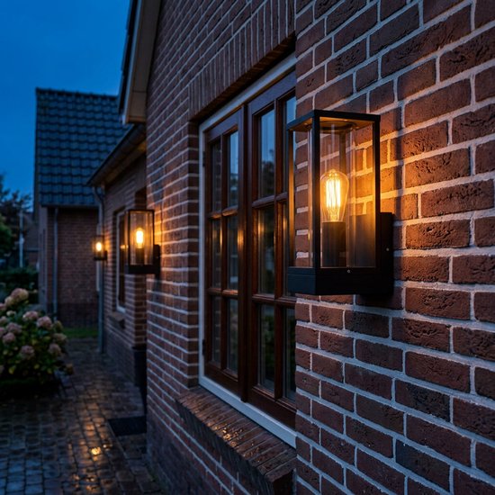 Zwarte wandlamp met glazen cilinder en zichtbare Edison-lamp, gemonteerd op bakstenen muur.