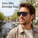 Man met donker haar, zonnebril met clip-on, zwart montuur, getint, met een beige jas, buiten. Geschikt voor autorijden, wandelen en vakantie.