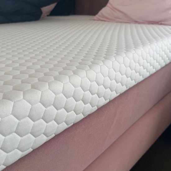Surmatelas blanc à motif hexagone sur un boxspring rose. Une partie d'un oreiller noir est visible.