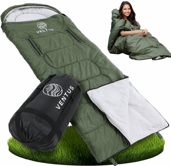 Groene slaapzak uitgevouwen met opgerolde slaapzak ernaast, en een vrouw in de slaapzak op de achtergrond.