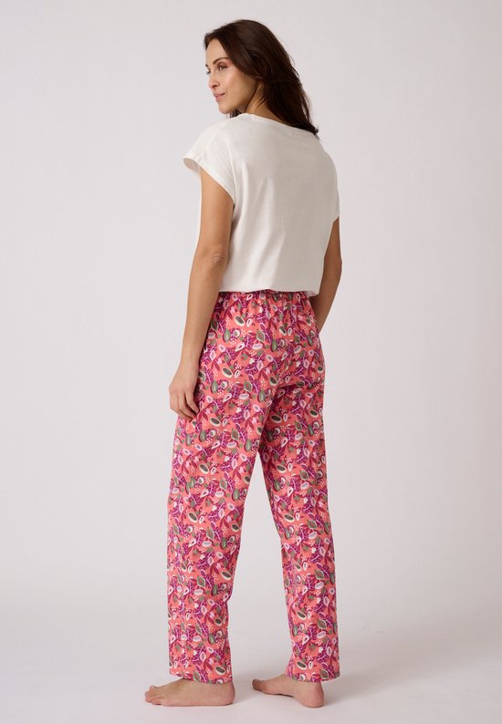 Vrouw van achteren gezien in een witte top en een roze pyjamabroek met tropische print.