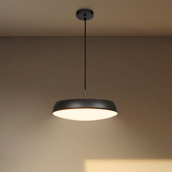 Donkergrijze hanglamp met plat, rond ontwerp en warm wit licht, hangend aan een zwart snoer.