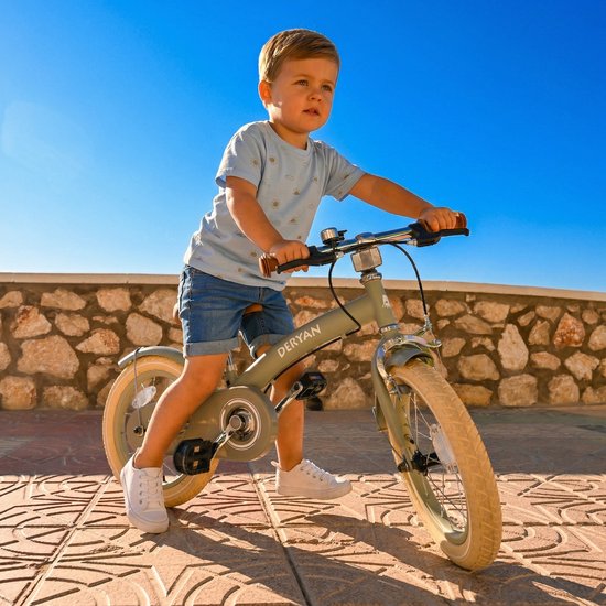 Garçon sur un vélo d'enfant vert Deryan avec poignées et selle marron, t-shirt bleu et short en jean.