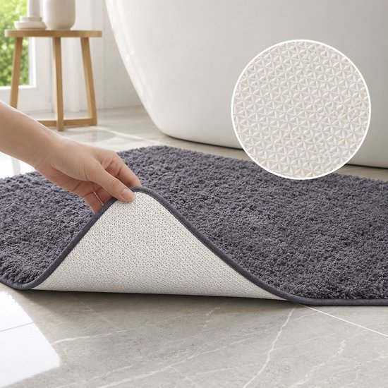 Hand toont de antislip TPR onderkant van een donkergrijze badmat met geometrisch patroon.