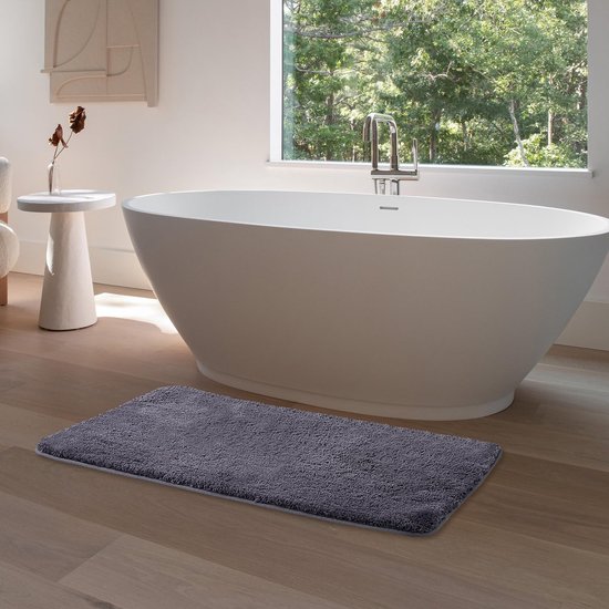 Donkergrijze badmat van microvezel op een houten vloer in een moderne badkamer met vrijstaand bad.