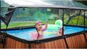 Twee kinderen met zwembrillen en zwembandjes in een rechthoekig zwembad met houtlook bekleding en zwarte rand, onder een transparante overkapping. Ze spelen met een groene en witte bal.
